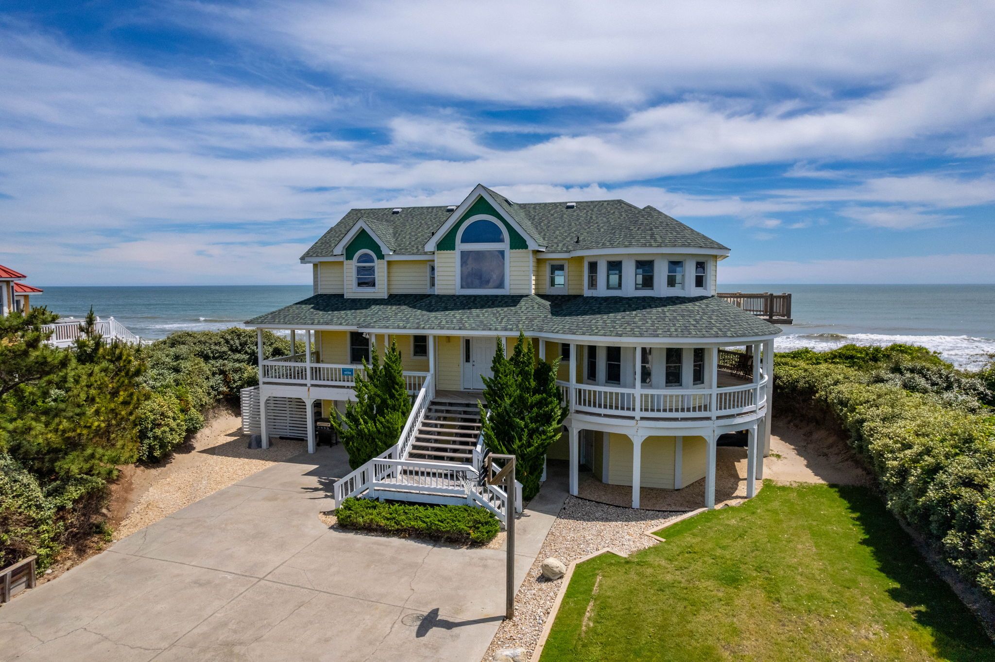 A two-story house with a balcony, a covered porch, and a view of the ocean.