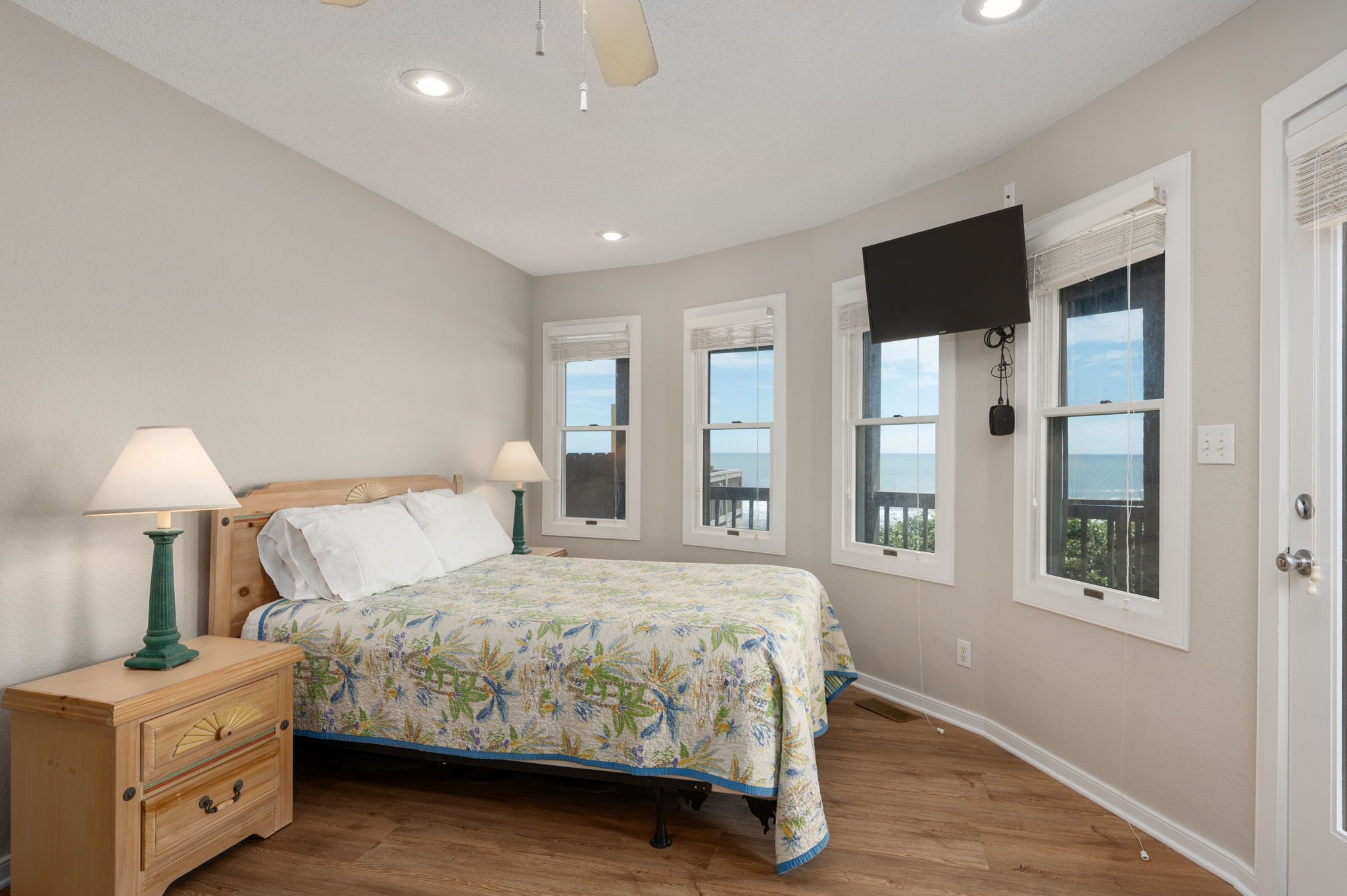 A bedroom with a bed, bedside tables, a ceiling fan, and windows with blinds.