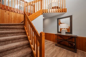 Eine Holztreppe mit Handlauf, Teppichstufen und einem Konsolentisch mit Lampe und Spiegel.