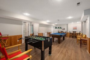 Ein Raum mit zwei Tischfußballtischen, Holzmöbeln und einem Billardtisch.