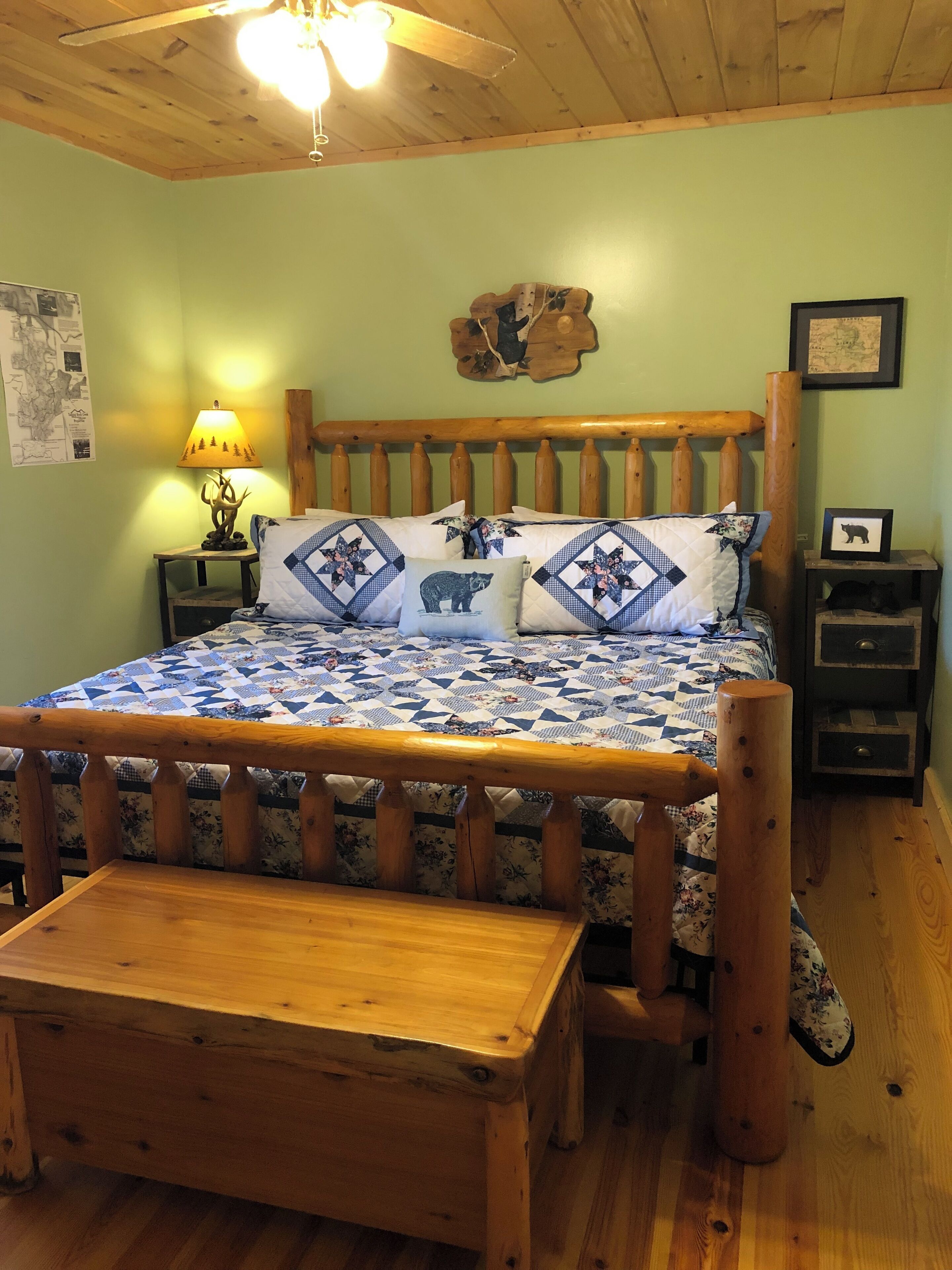 A wooden bed with a quilt, a nightstand with a lamp, and a wall map.
