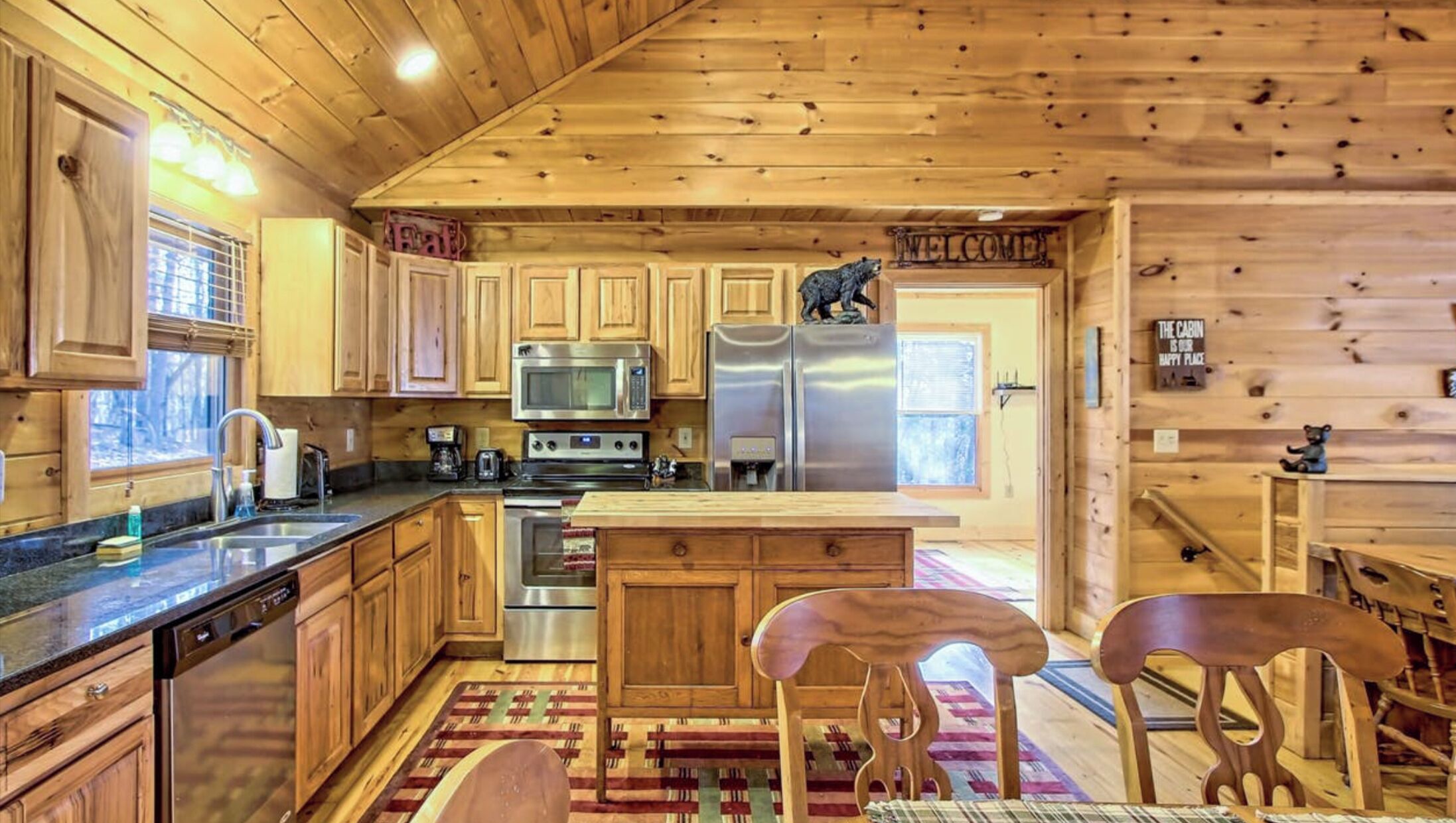 A cabin-style kitchen with wooden cabinets, stainless steel appliances, and a central island with stools.