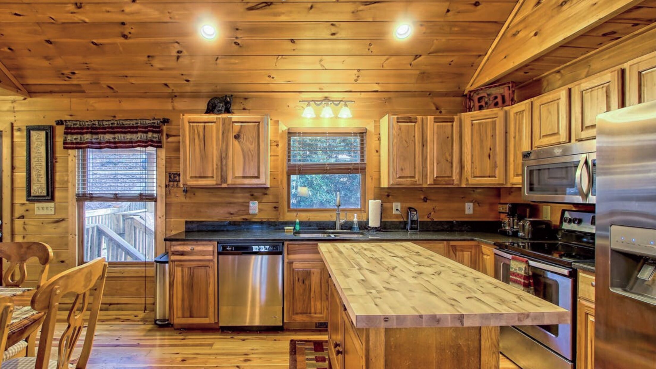 Cocina de cabaña de madera con una isla central, electrodomésticos de acero inoxidable y ventana con vista a una terraza.