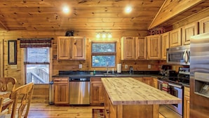A wooden cabin kitchen with a central island, stainless steel appliances, and a window overlooking a deck.
