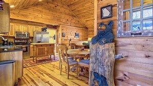 A cabin interior with wooden walls, a kitchen with stainless steel appliances, a dining area with a table and chairs, and a bear sculpture.