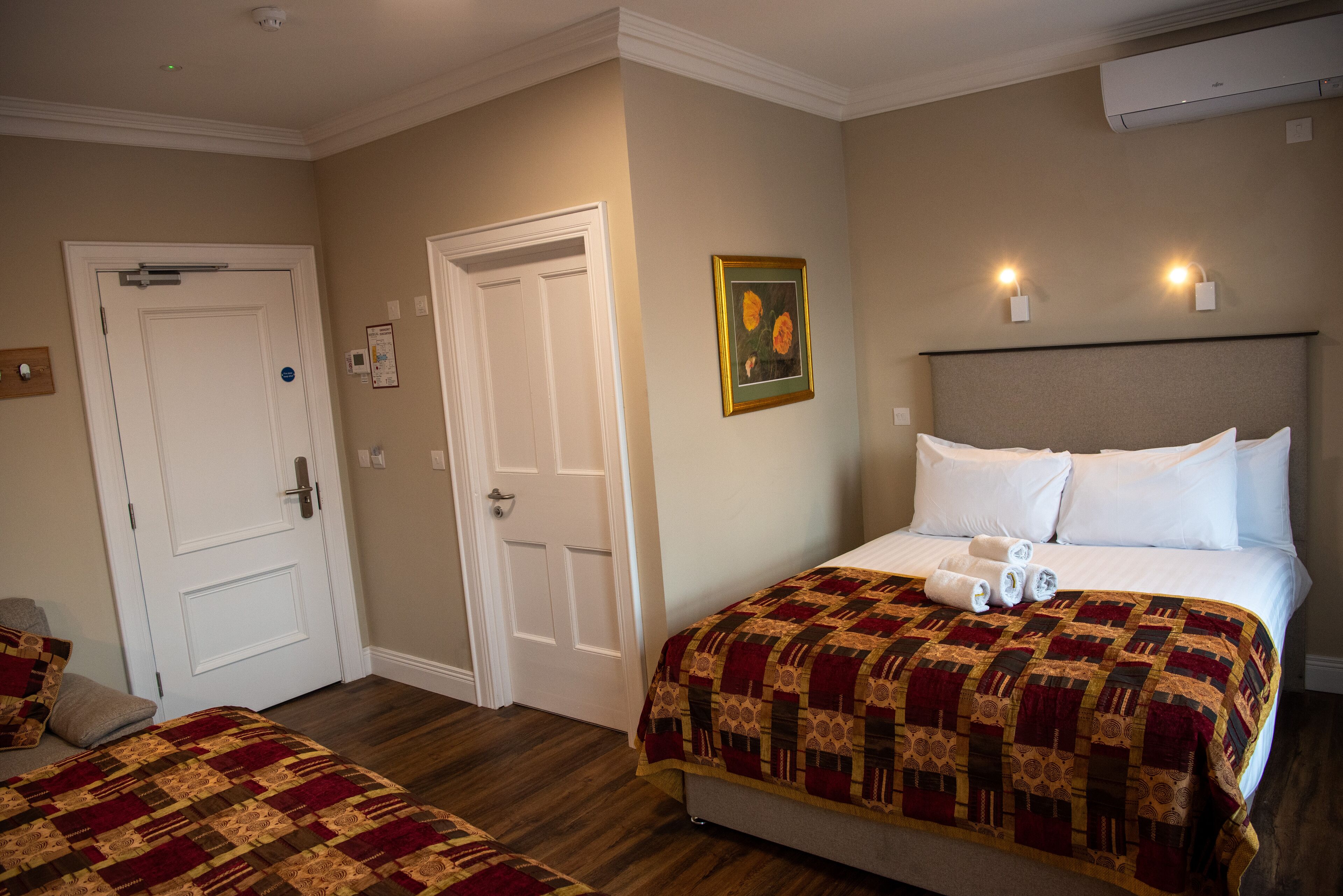 A hotel room with a large bed, a smaller bed, a door, and a painting on the wall.