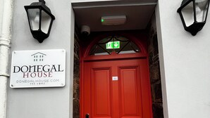 Une porte rouge avec une enseigne au-dessus indiquant « Donegal House » et une adresse de site web.