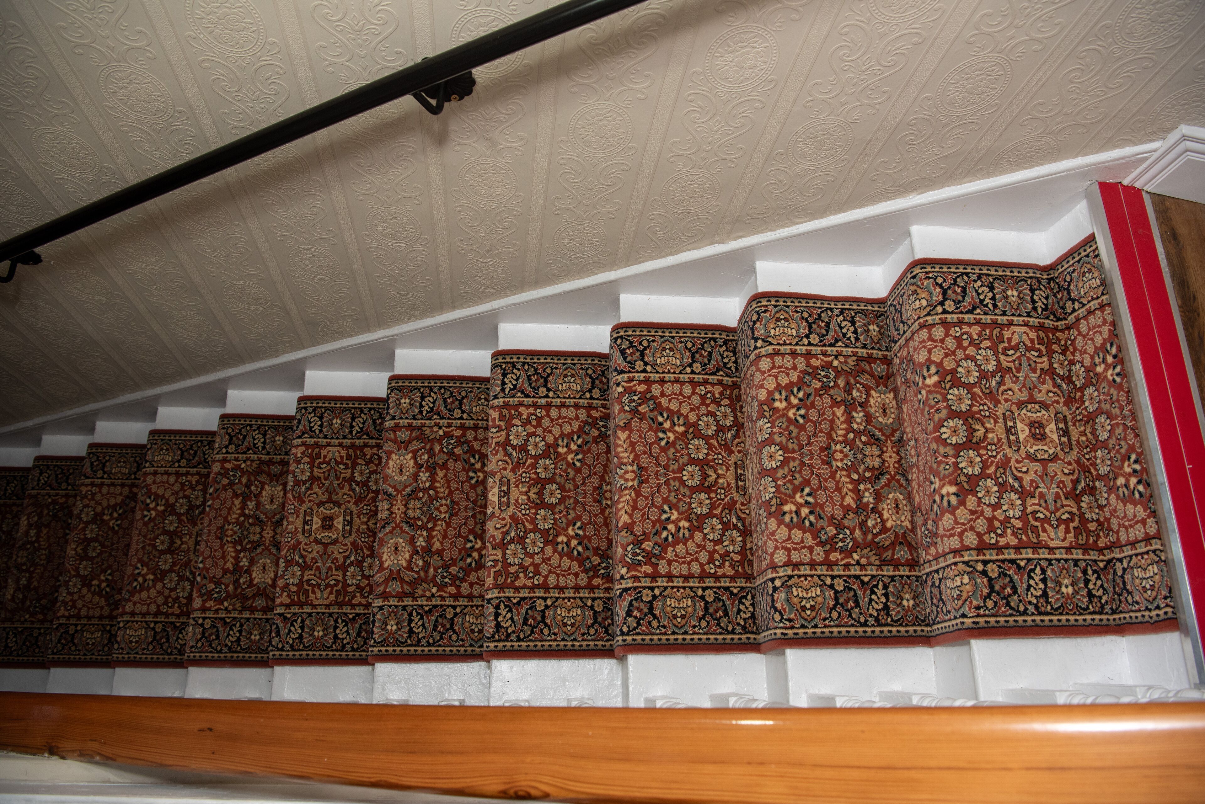 A staircase with ornate, patterned carpet and white walls.