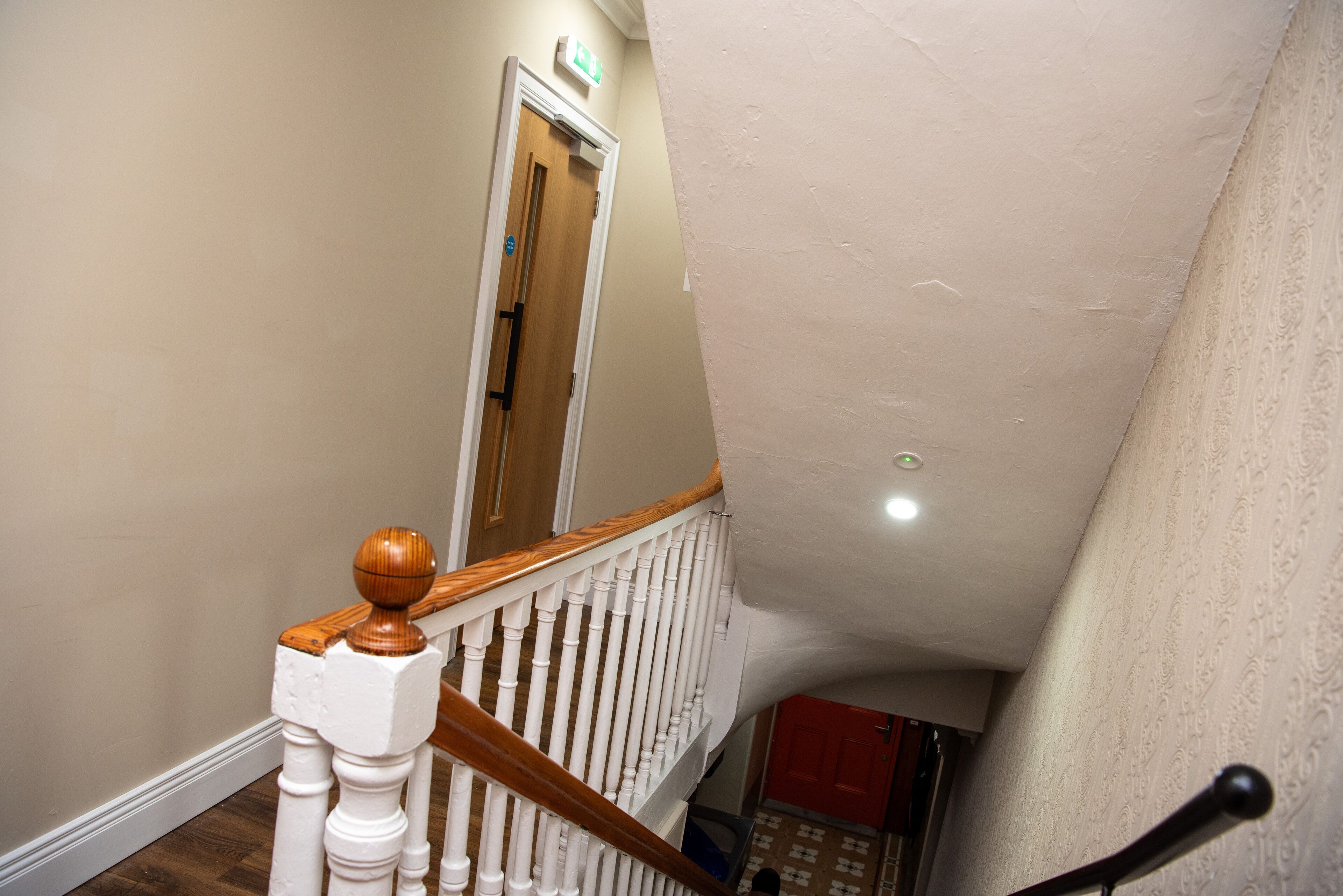 A staircase with white balusters and wooden handrails, leading to a door with a green exit sign.