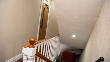 A staircase with white balusters and wooden handrails, leading to a door with a green exit sign.