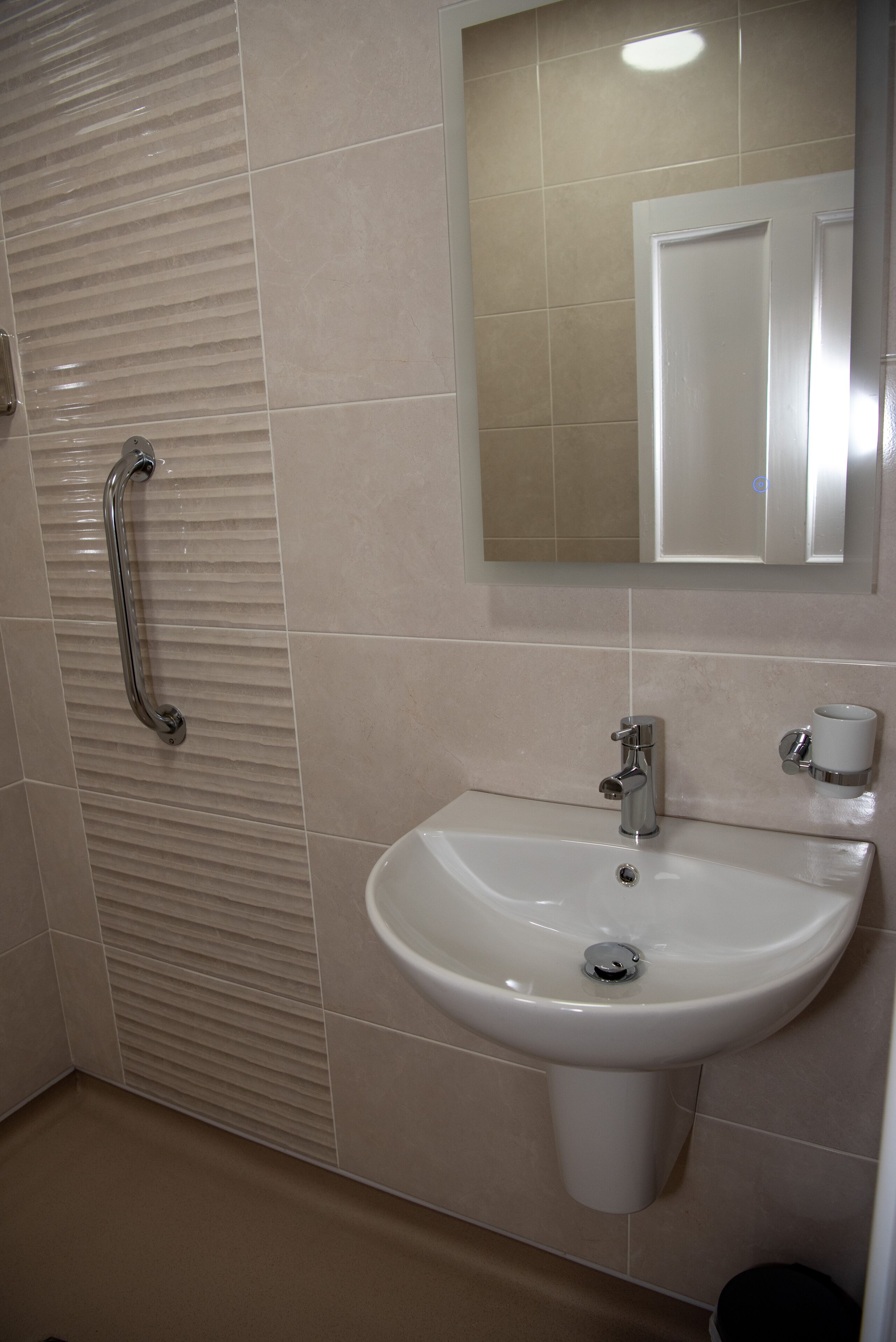 A bathroom with a sink, mirror, and handrail.
