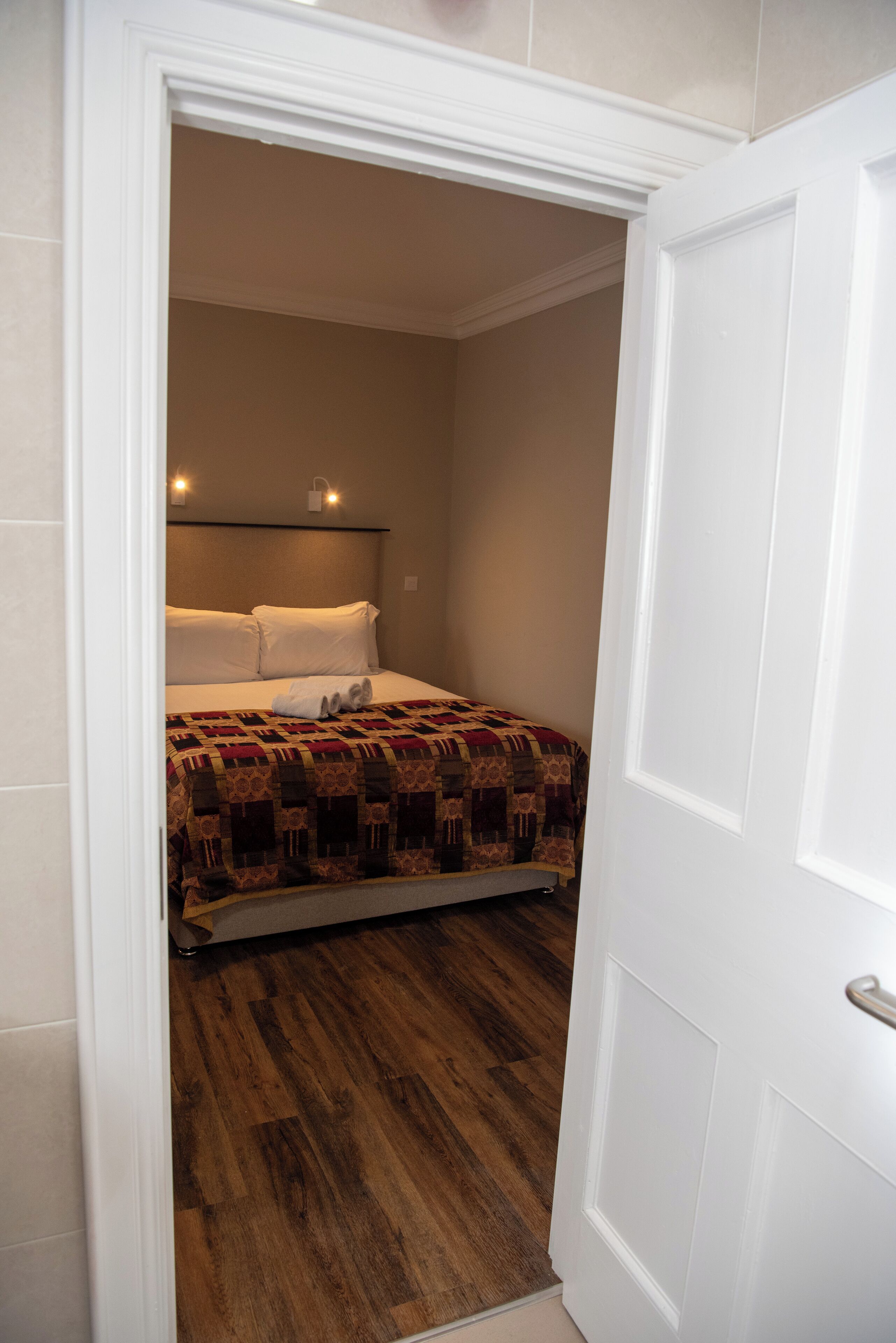 A bedroom with a wooden floor, a bed with a patterned bedspread, and a white door.