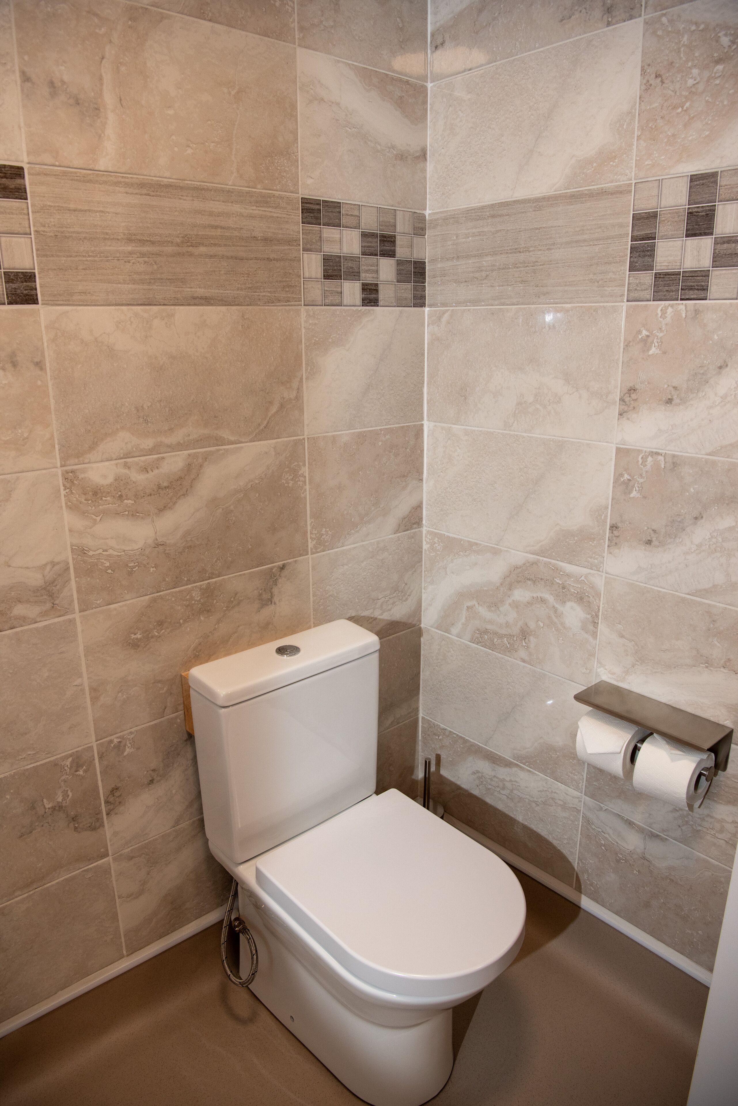 A bathroom with a toilet, a toilet paper holder, and a marble-tiled wall.
