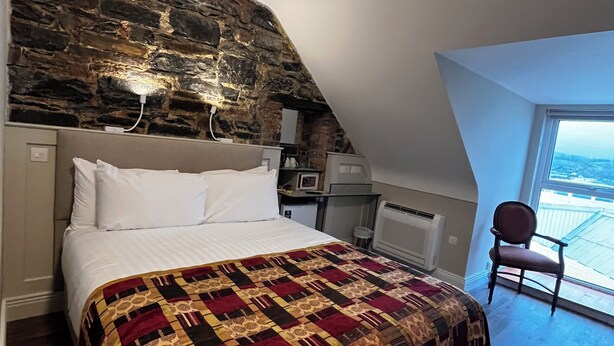 Une chambre avec un grand lit, un mur en pierre, une chaise et une vue par la fenêtre.