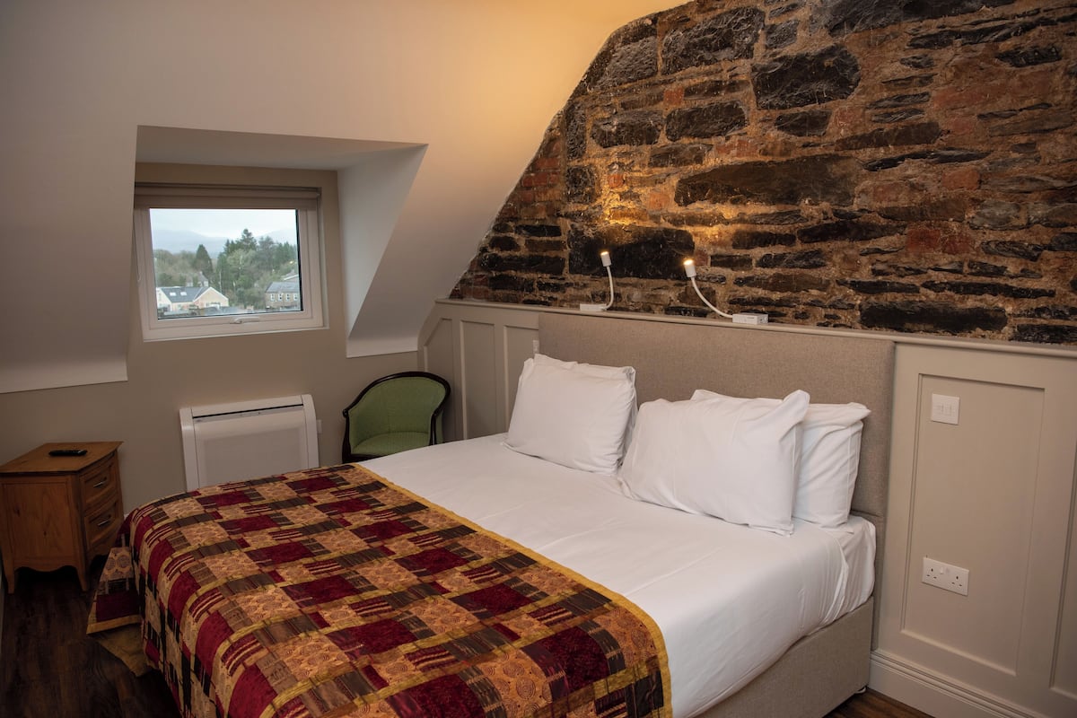 A bedroom with a large bed, a stone wall, a window, a radiator, and a chair.