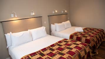 Two single beds with white linens and a patterned blanket, headboards with wall-mounted lights, and a neutral-colored wall.