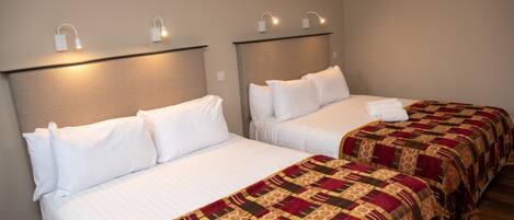 Two single beds with white linens and a patterned blanket, headboards with wall-mounted lights, and a neutral-colored wall.