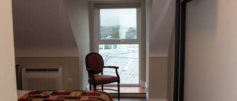 Un dormitorio con una cama grande, una silla, un televisor montado en la pared y un ventanal con vistas al exterior.