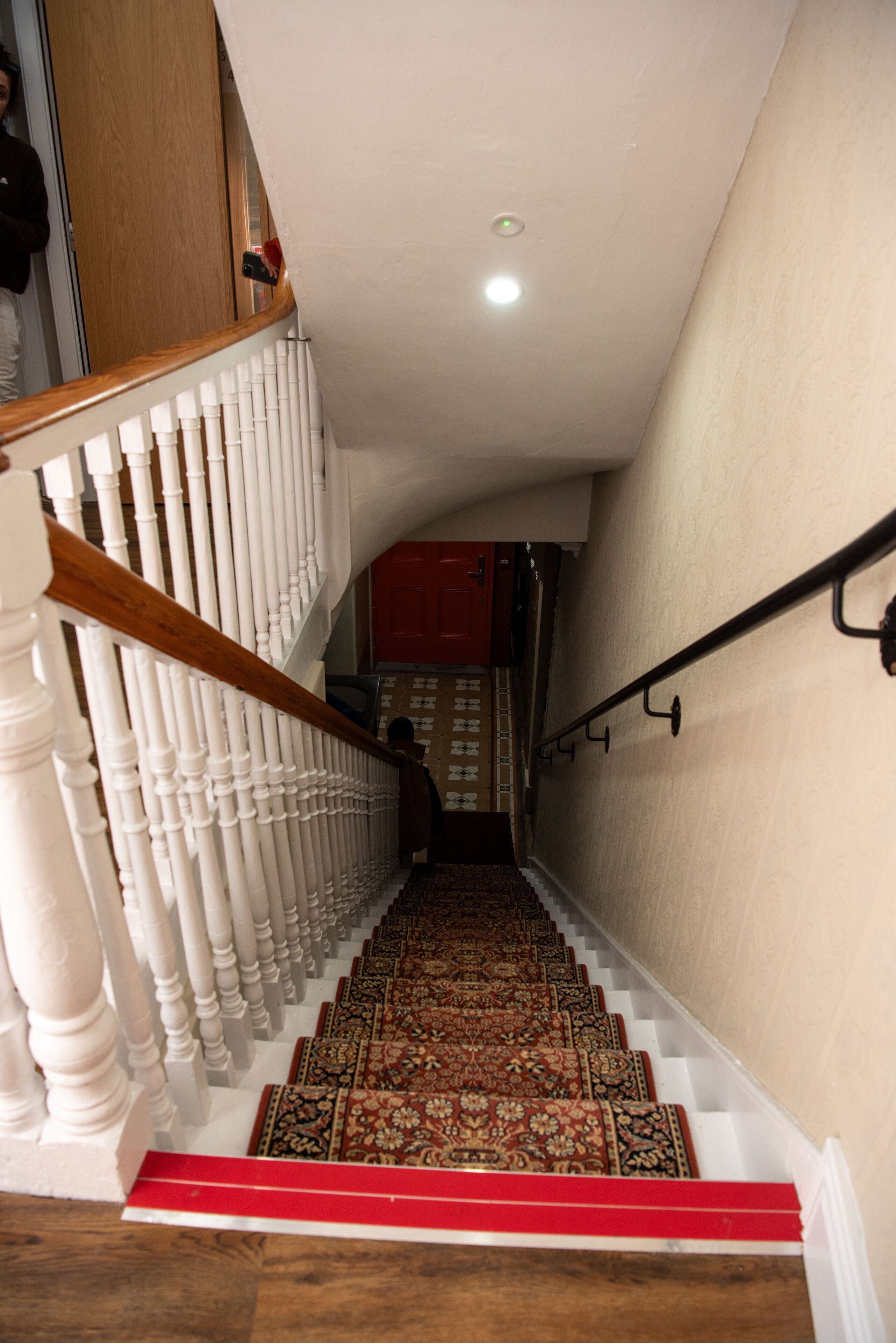 Una escalera con balaustres blancos, alfombra roja y barandilla de madera.
