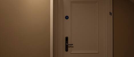 A narrow hallway with a white door, a red emergency light, and a ceiling light.