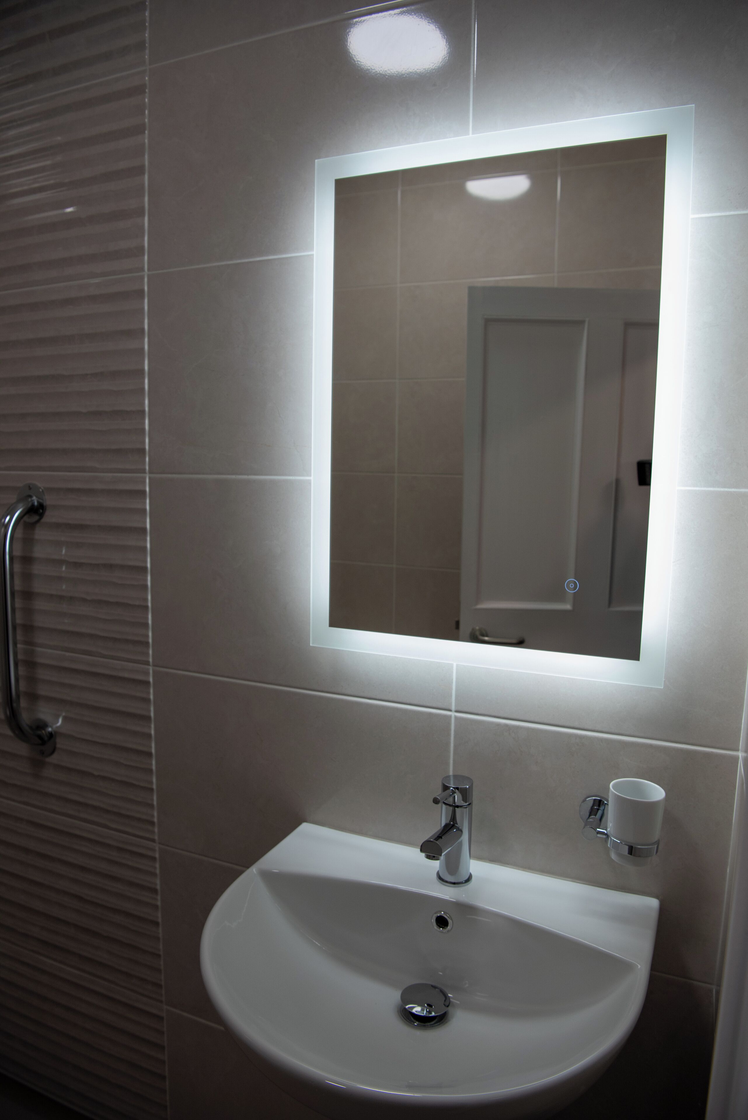 A bathroom with a white sink, a mirror, and a handrail.