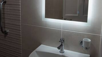 A bathroom with a white sink, a mirror, and a handrail.