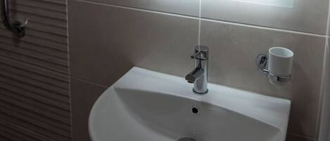 A bathroom with a white sink, a mirror, and a handrail.