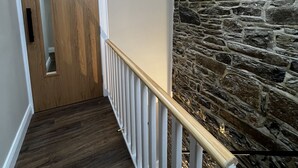 Un couloir avec une porte en bois, un mur en pierre et une rambarde en bois.