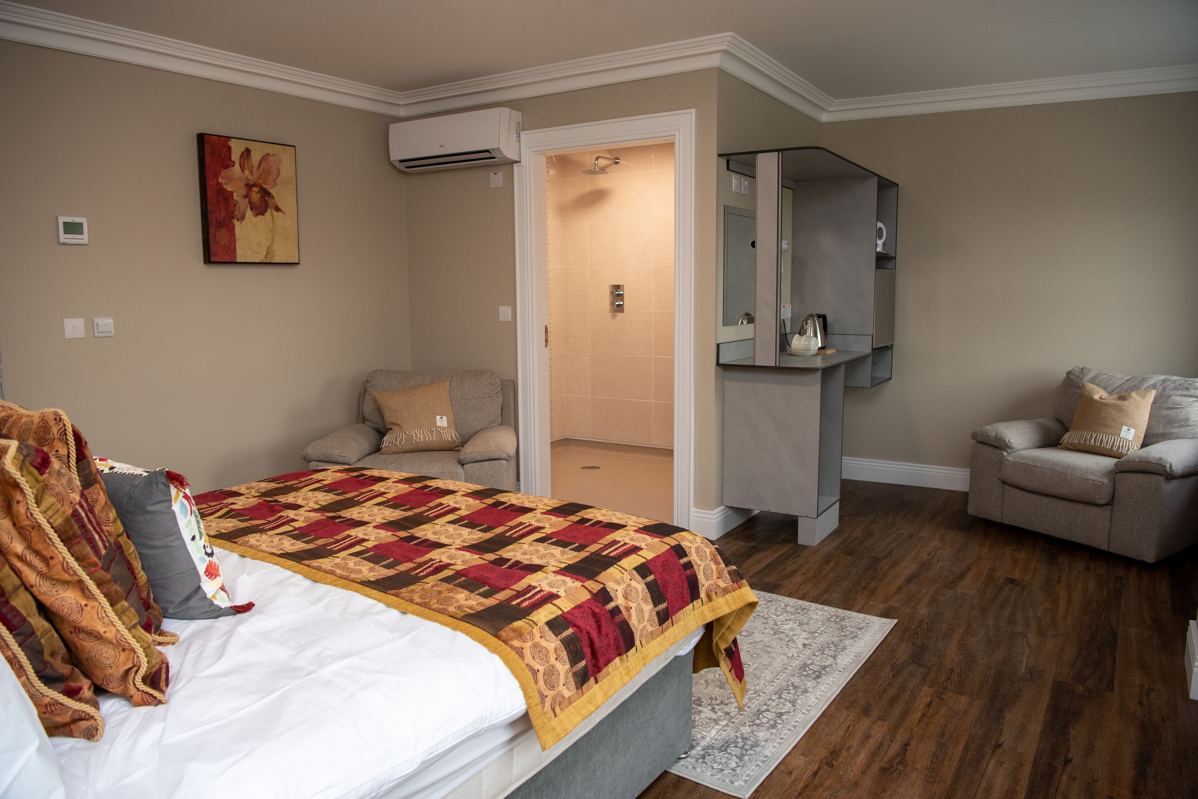 Un dormitorio con una cama grande, un sofá gris, un sillón pequeño, un espejo y una zona de ducha.