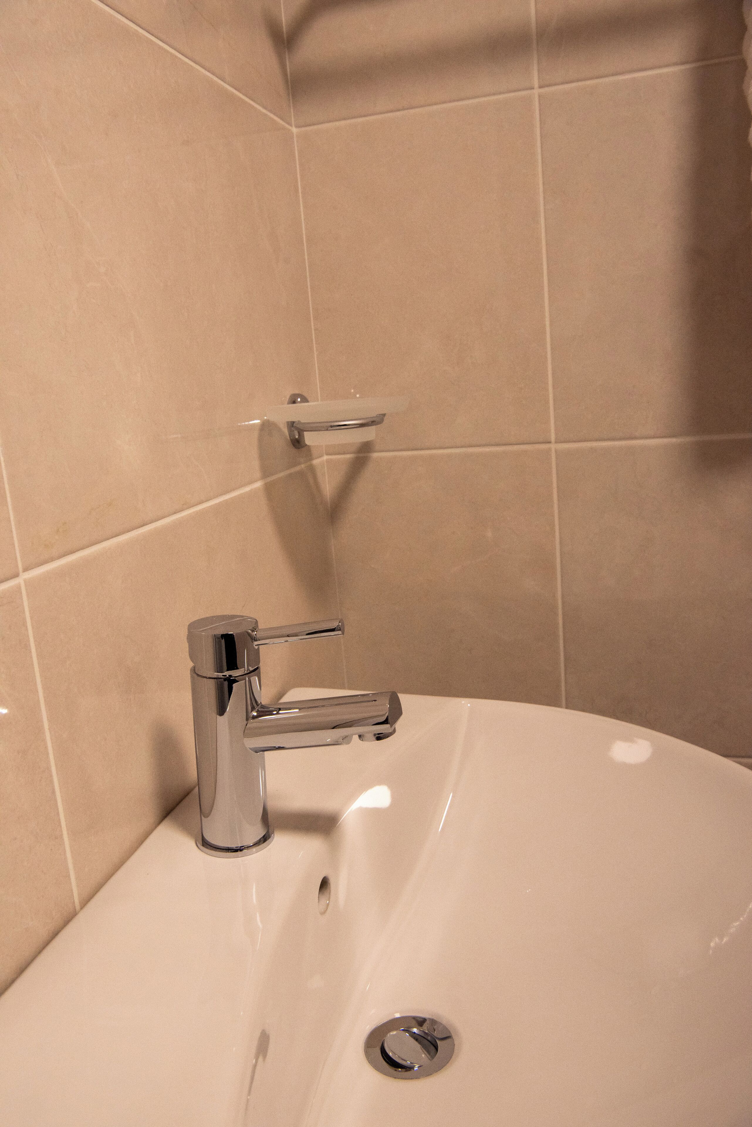 Un baño con lavamanos blanco, grifo cromado y un perchero para toallas.