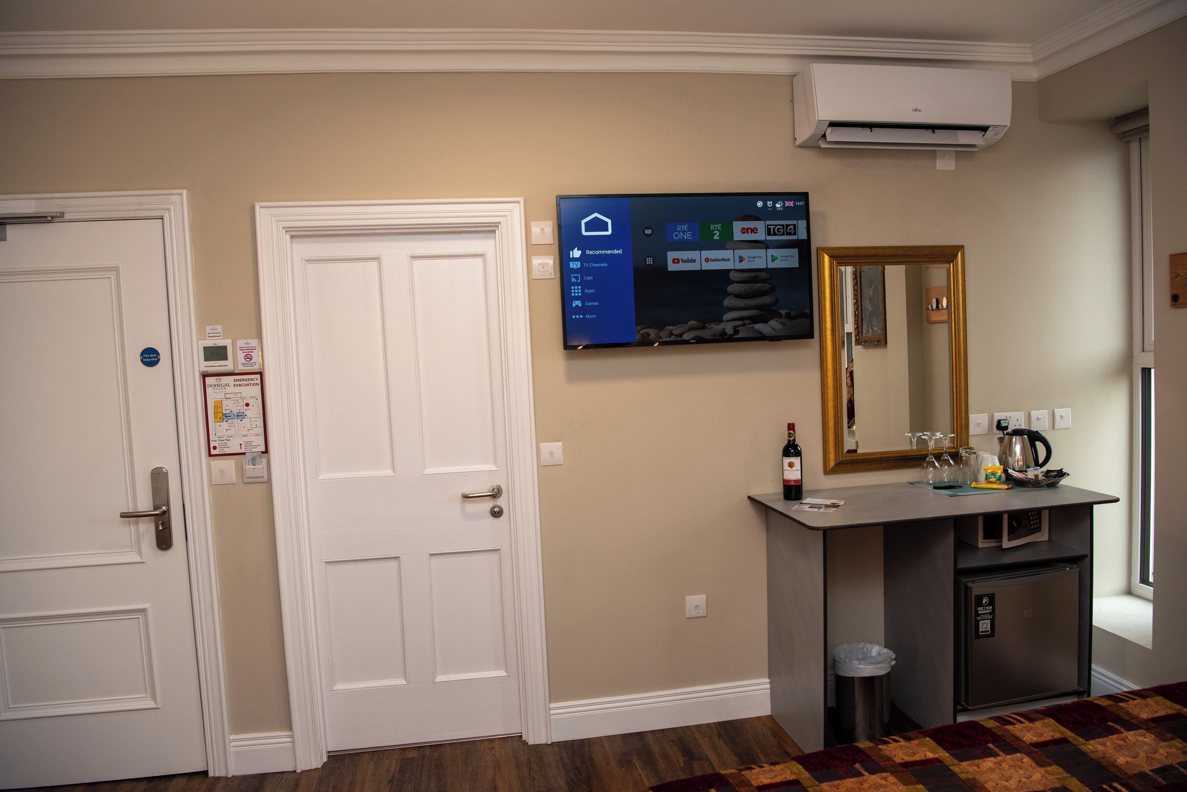 Habitación de hotel con televisión de pantalla plana montada en la pared, minibar, refrigerador pequeño y ventana con vistas.