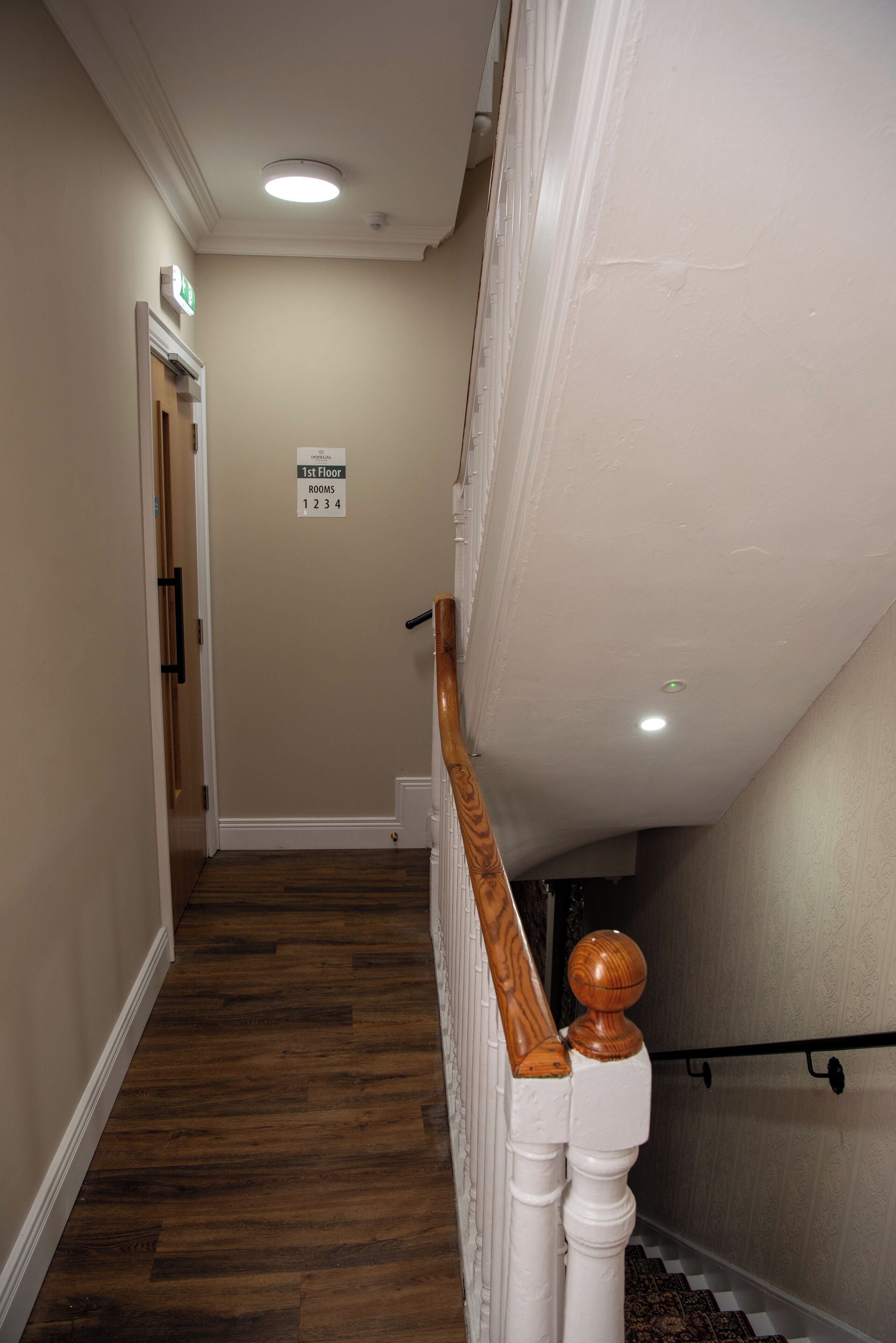 A hallway with a wooden floor, white walls, and a sign indicating room numbers.