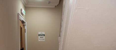 A hallway with a wooden floor, white walls, and a sign indicating room numbers.