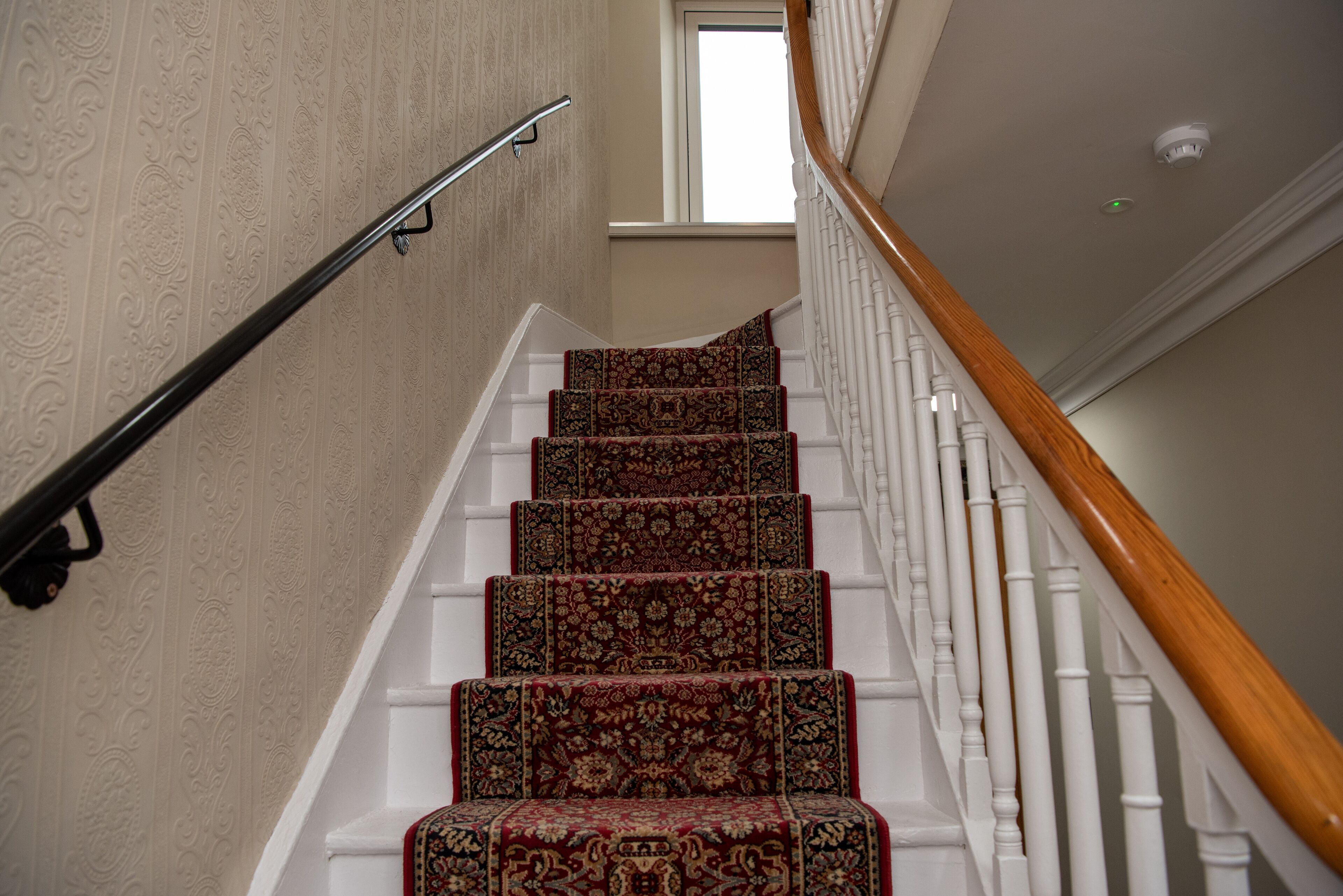 Un escalier avec des marches recouvertes d’une moquette décorative et des rampes blanches.
