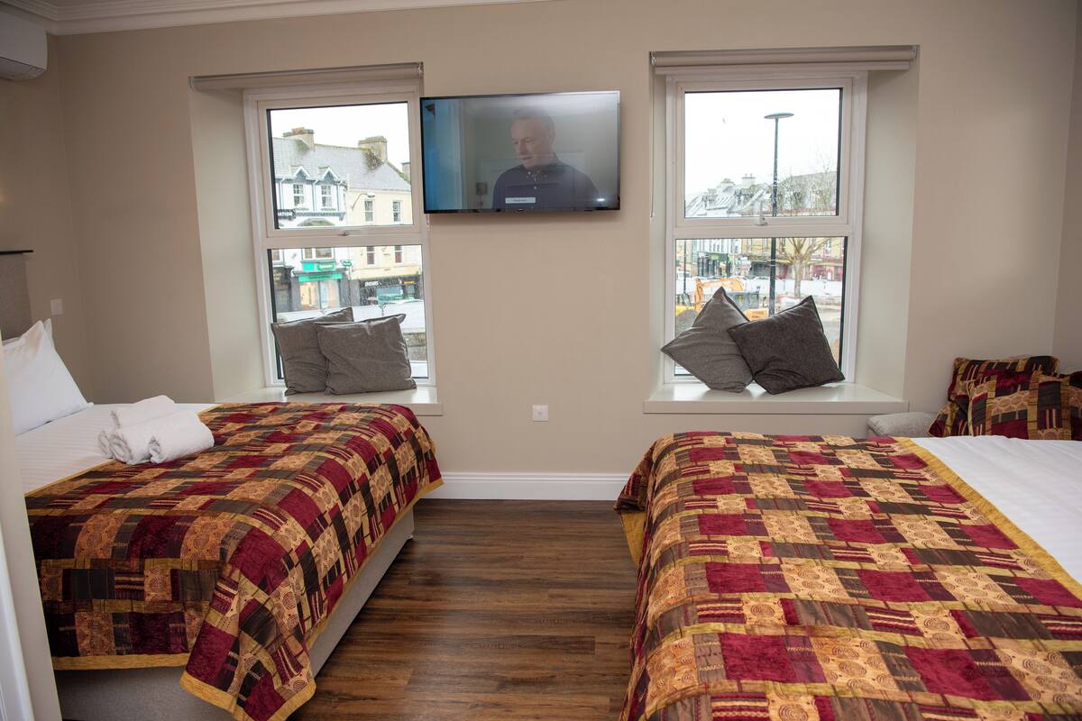 A hotel room with two beds, a TV mounted on the wall, and windows with views of the outside.