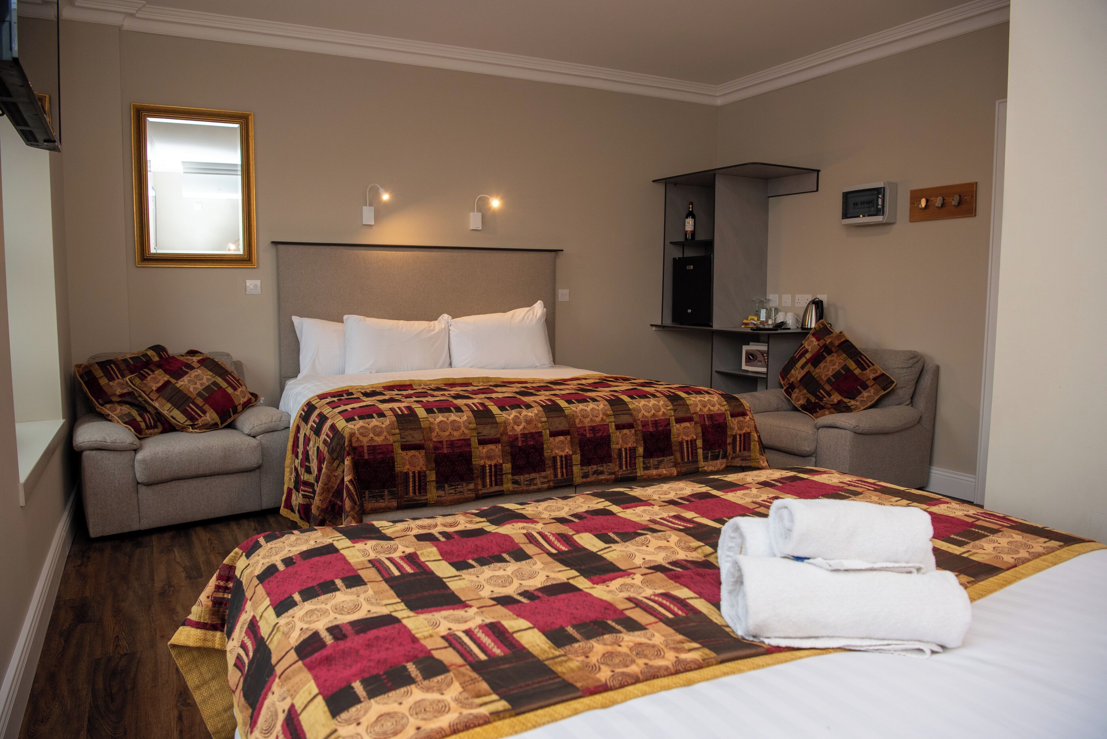 A hotel room with a large bed, two armchairs, a small table with a microwave, and a mirror on the wall.