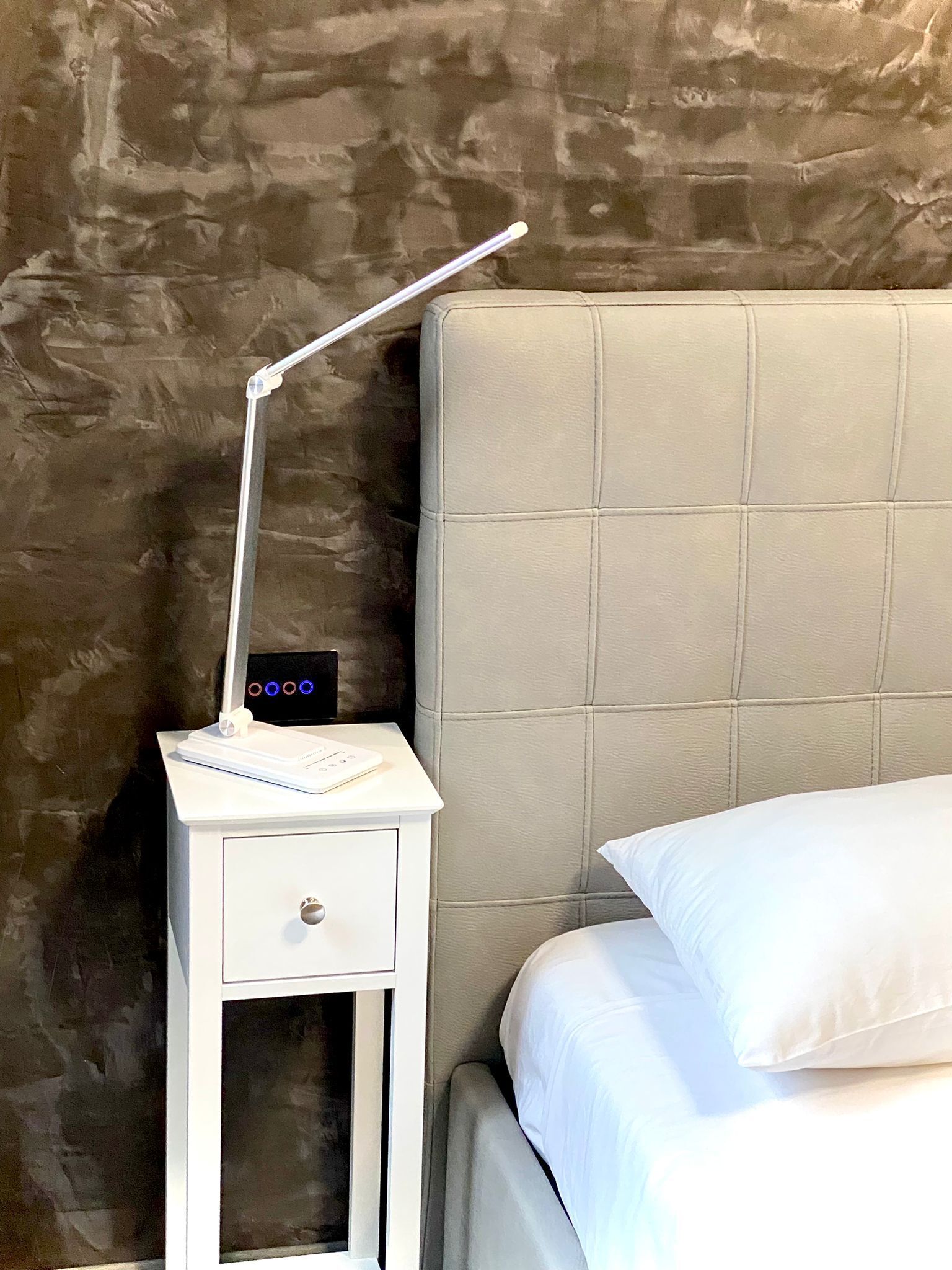 A bed with a headboard, a bedside table with a lamp, and a wall with a textured pattern.