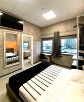 Camera d'albergo moderna con un letto grande, una scrivania, uno specchio e una finestra vista esterna.