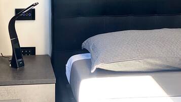 A modern hotel room with a large bed, a bedside table with a lamp, and a wall-mounted control panel.