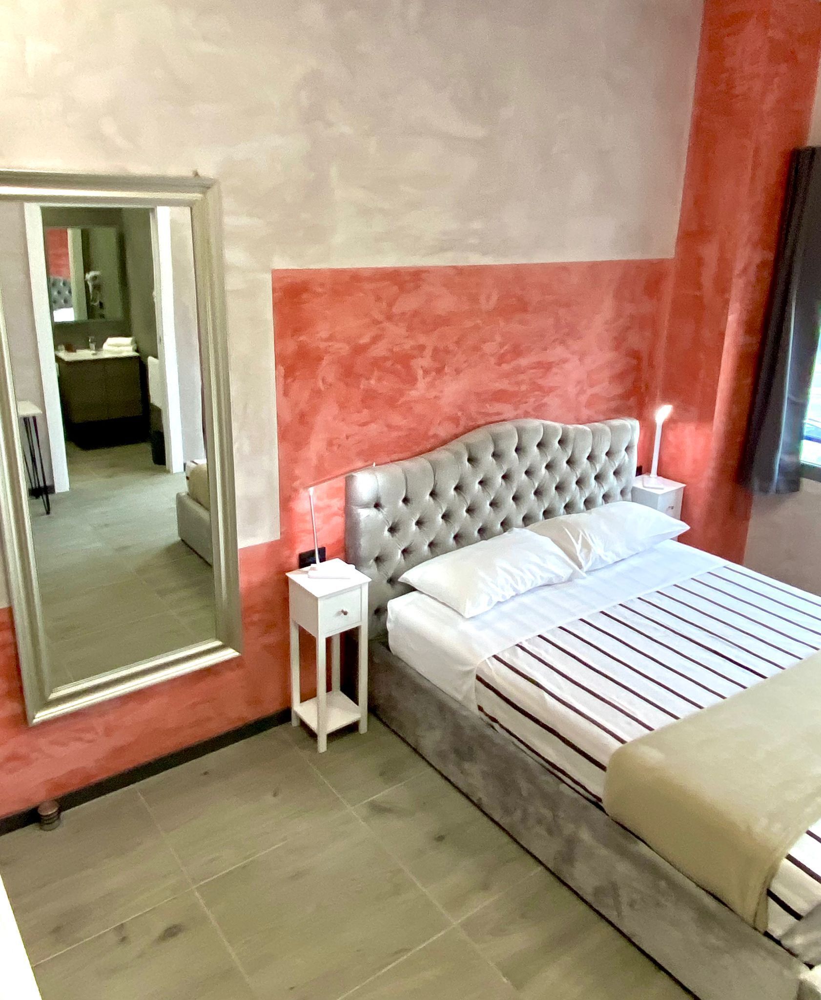 A bedroom with a large bed, a nightstand, a mirror, and a view of a bathroom.