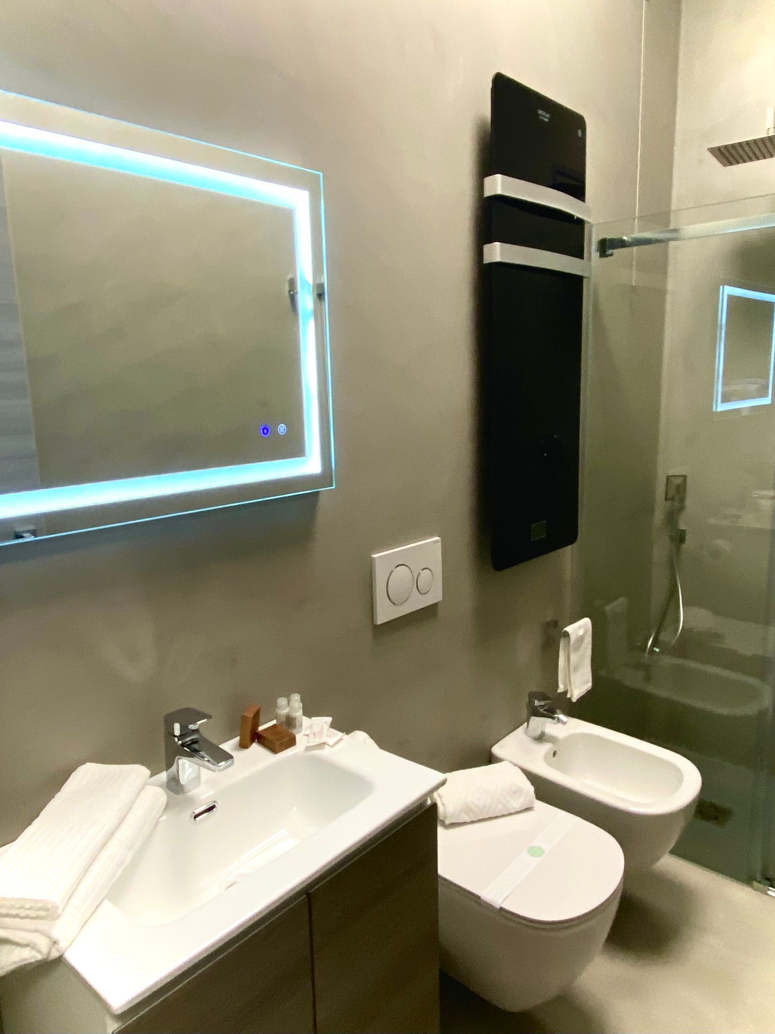 Ein modernes Badezimmer mit großem Spiegel, Waschbecken, zwei Bidets und einer Duschkabine aus Glas.