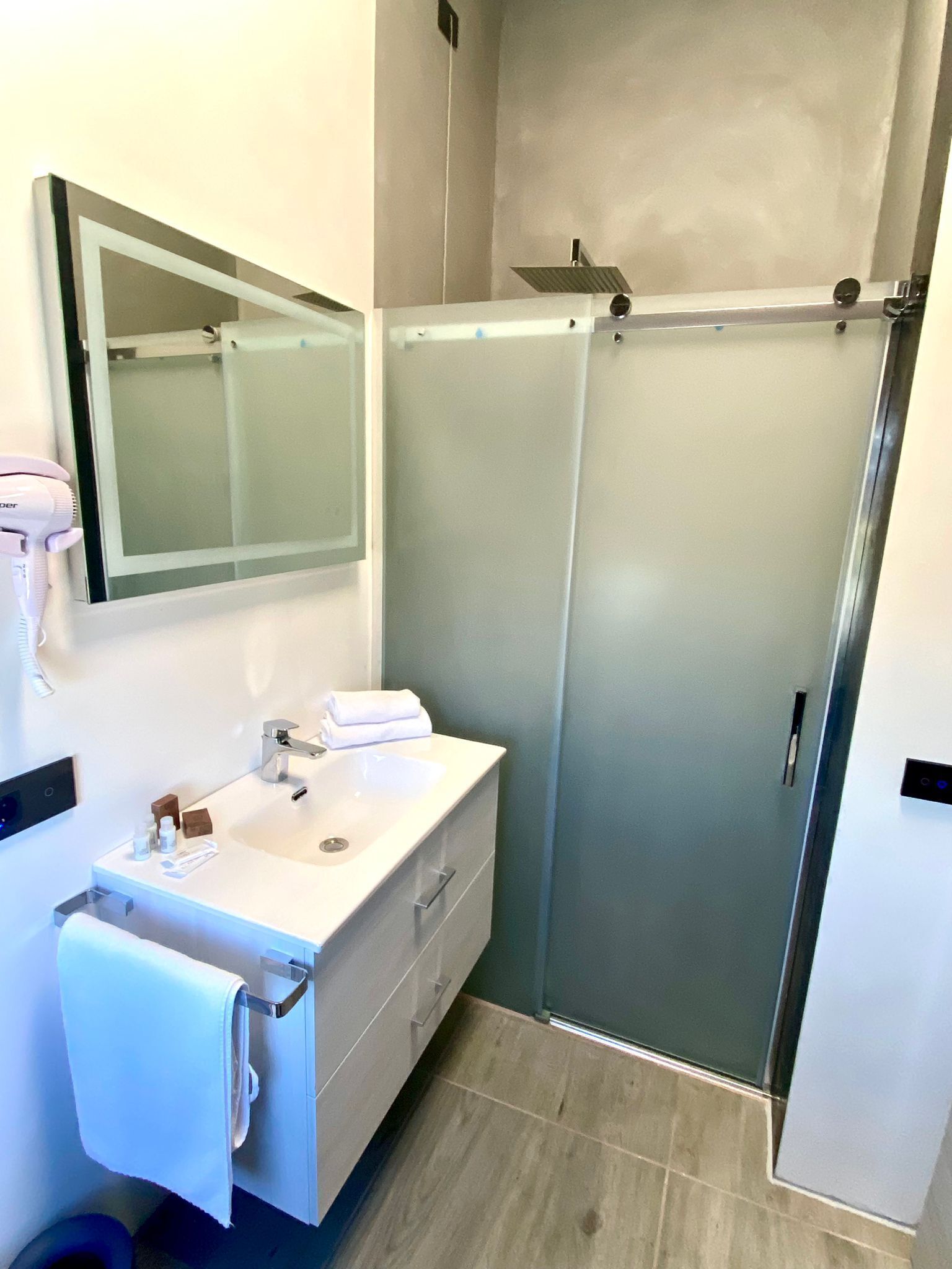 Une salle de bain moderne avec une douche à parois de verre, un meuble-lavabo blanc avec un miroir et un porte-serviettes.