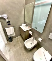Un bagno moderno con bidet, WC, lavabo, specchio e asciugacapelli.