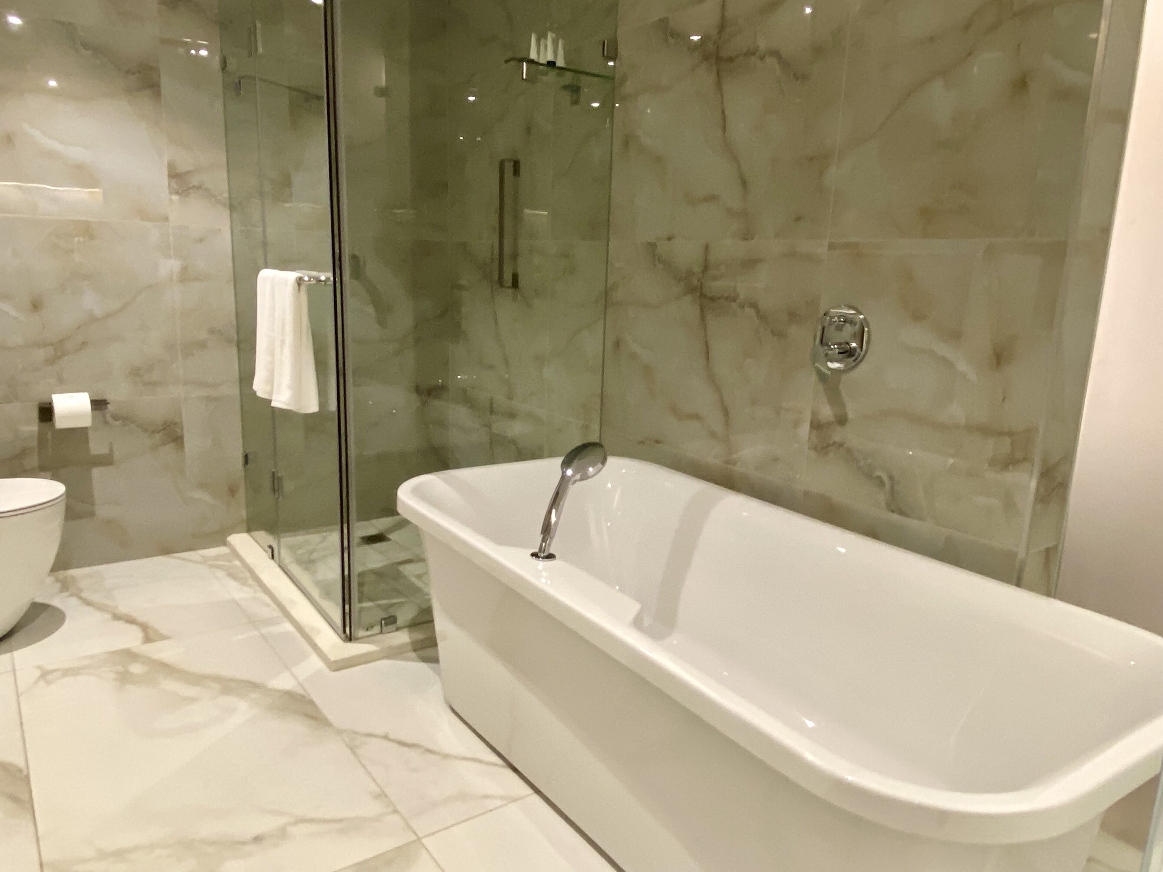 A modern bathroom with a freestanding bathtub, a glass shower enclosure, and marble flooring.