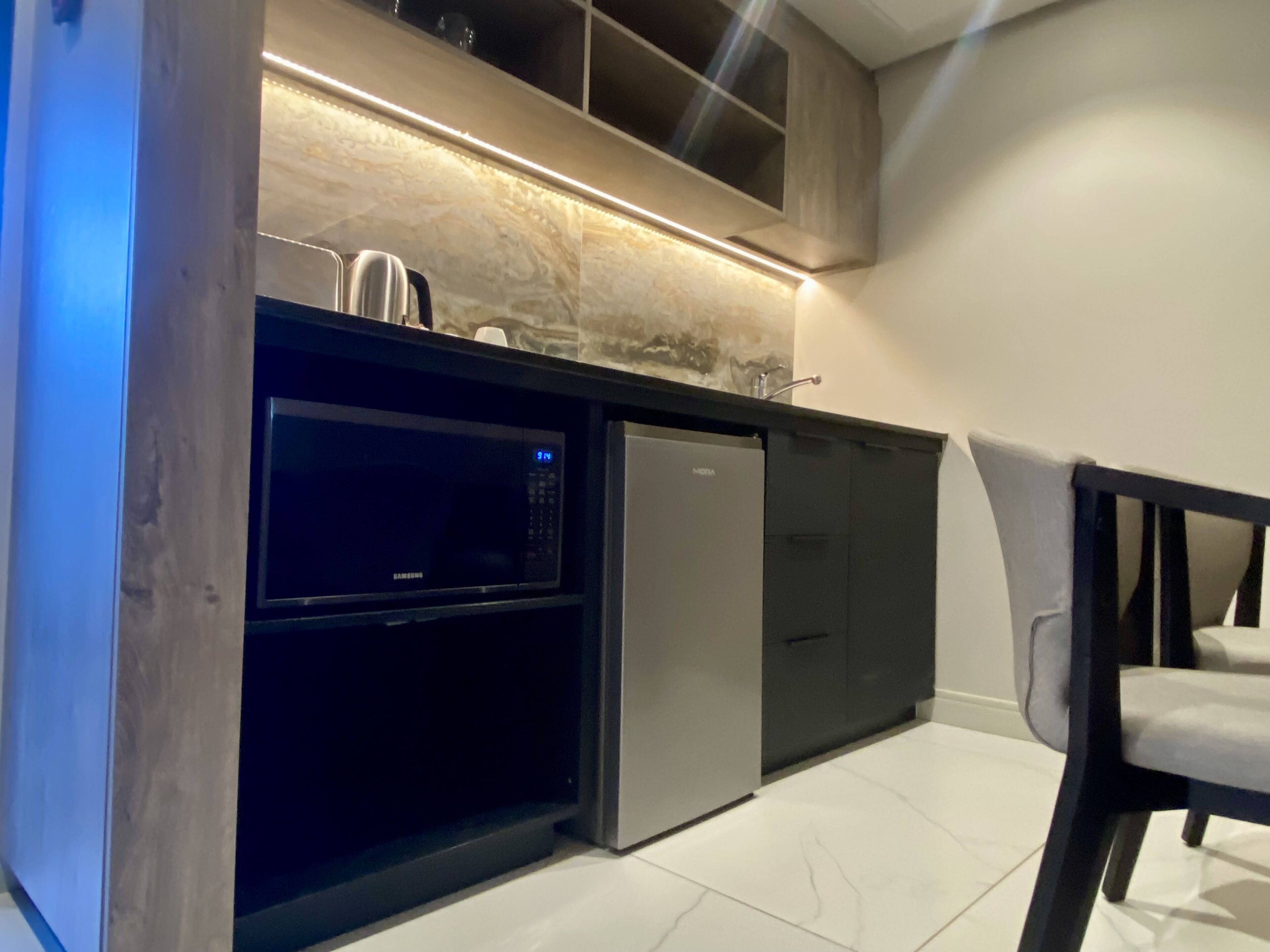 A compact kitchen with a microwave, refrigerator, and a chair.