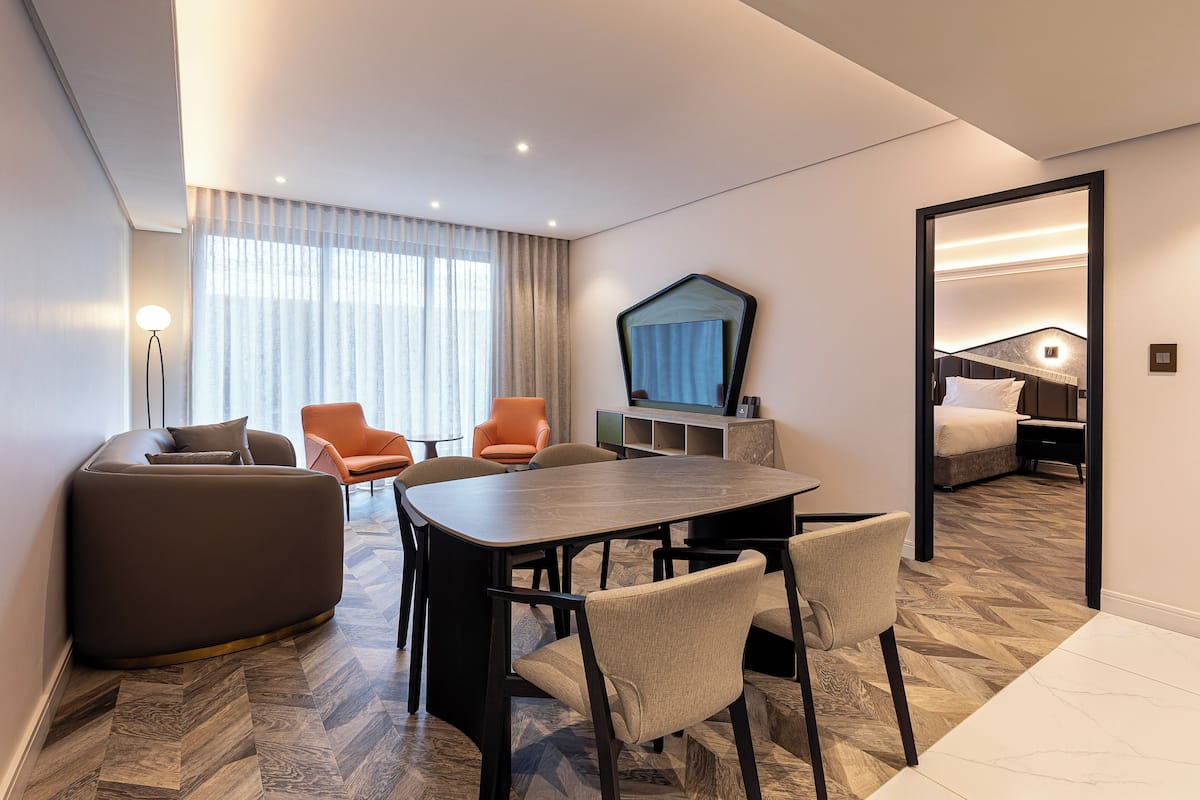 A modern hotel room with a dining area, a sofa, and a bed.