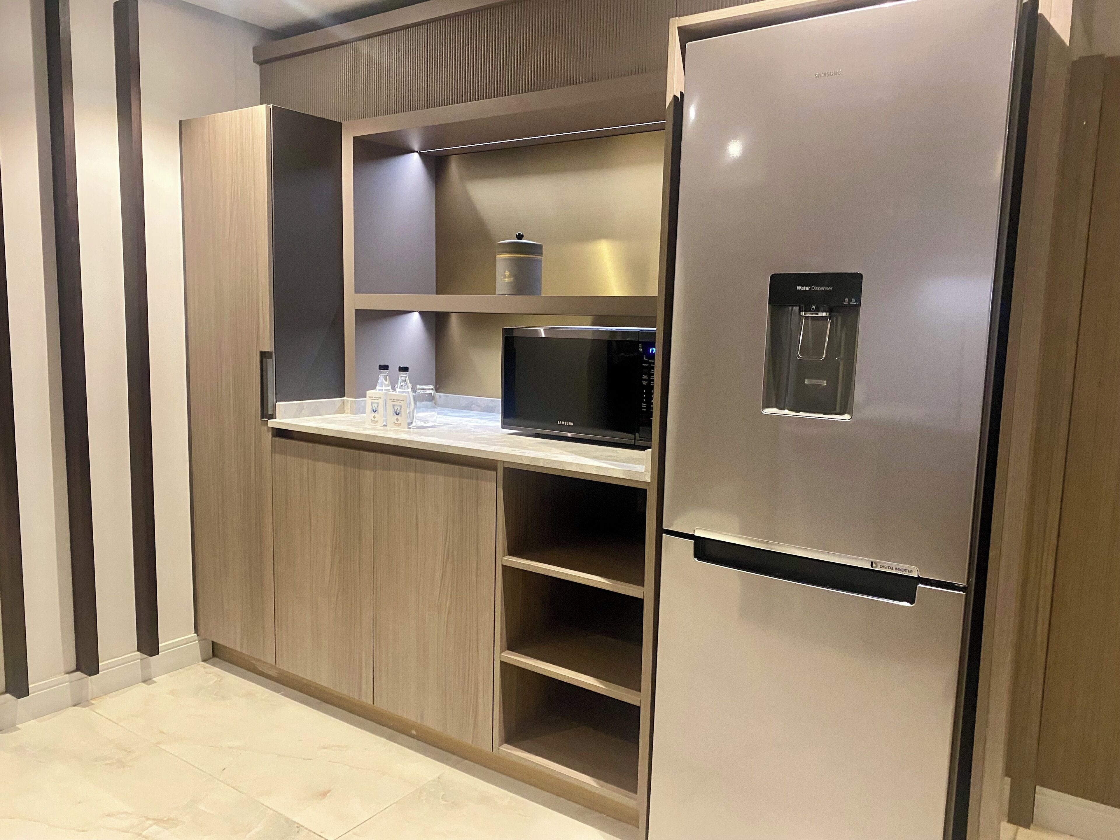 A modern kitchen with a built-in microwave, a water dispenser, and a stainless steel refrigerator.