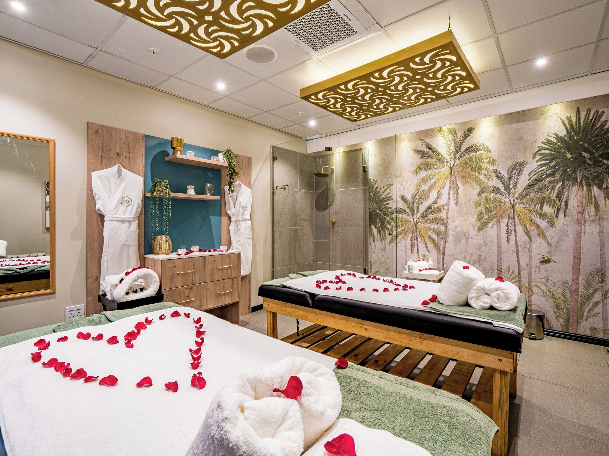 A spa room with two massage tables, a wooden cabinet, a mirror, and a shower area.