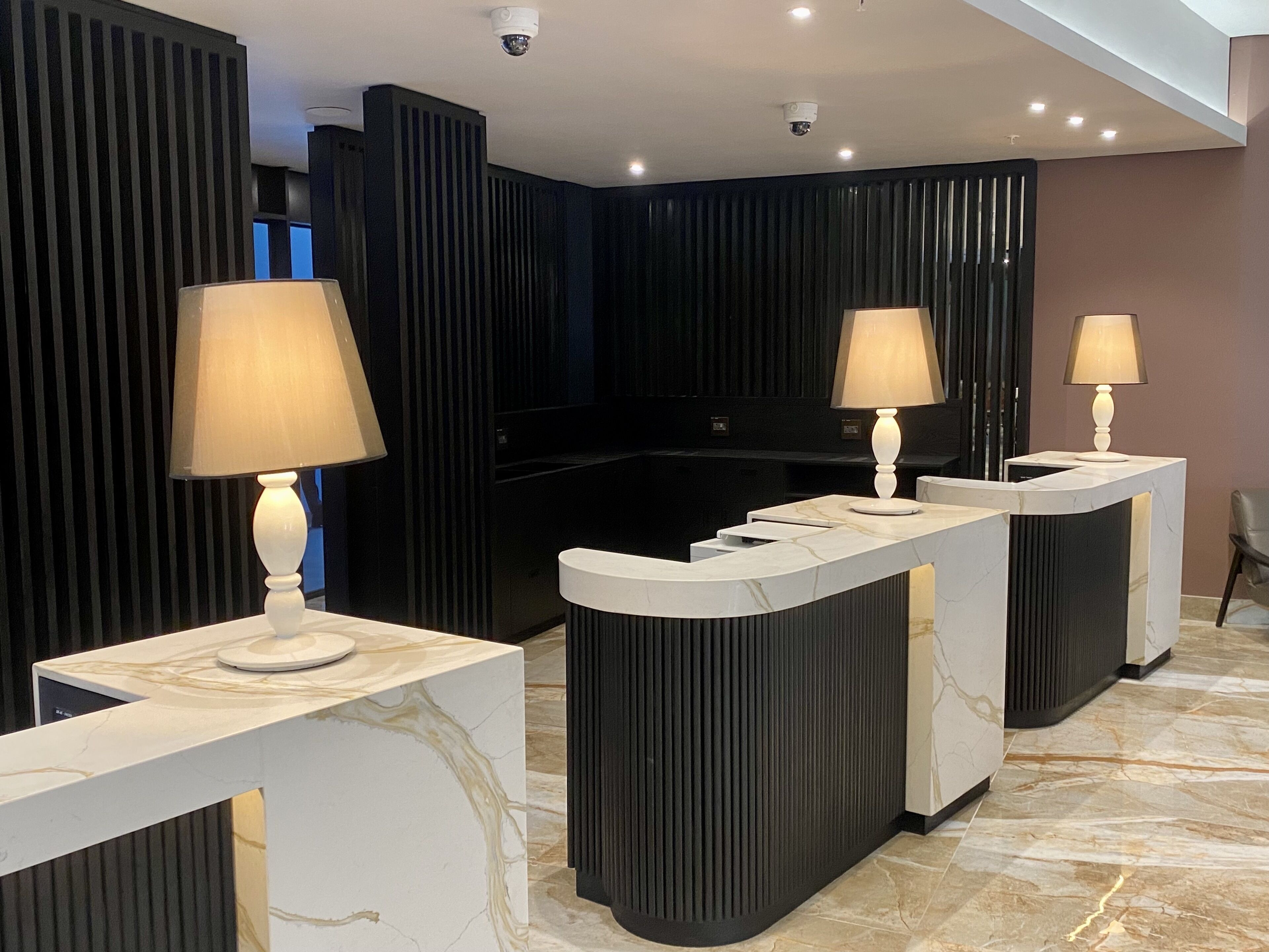 A reception area with marble counters, black acoustic panels, and three standing lamps.