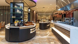 Un moderno vestíbulo de hotel con un mostrador central, vitrinas de vidrio y una pared de ladrillo con zona de cocina.